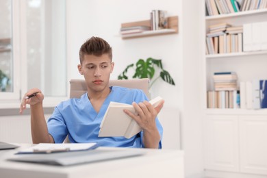 Photo of Medical student with book studying at table indoors