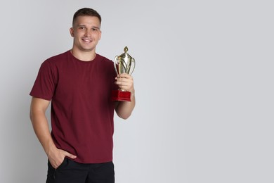 Happy winner with golden trophy cup on light grey background, space for text