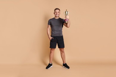 Photo of Happy winner with golden trophy cup on beige background