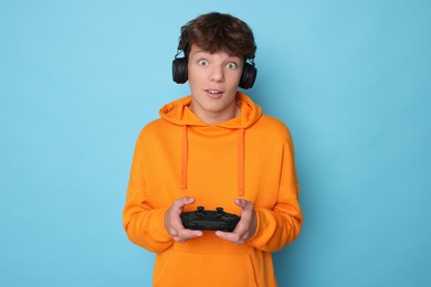 Teenage boy in headphones playing video game with controller on light blue background