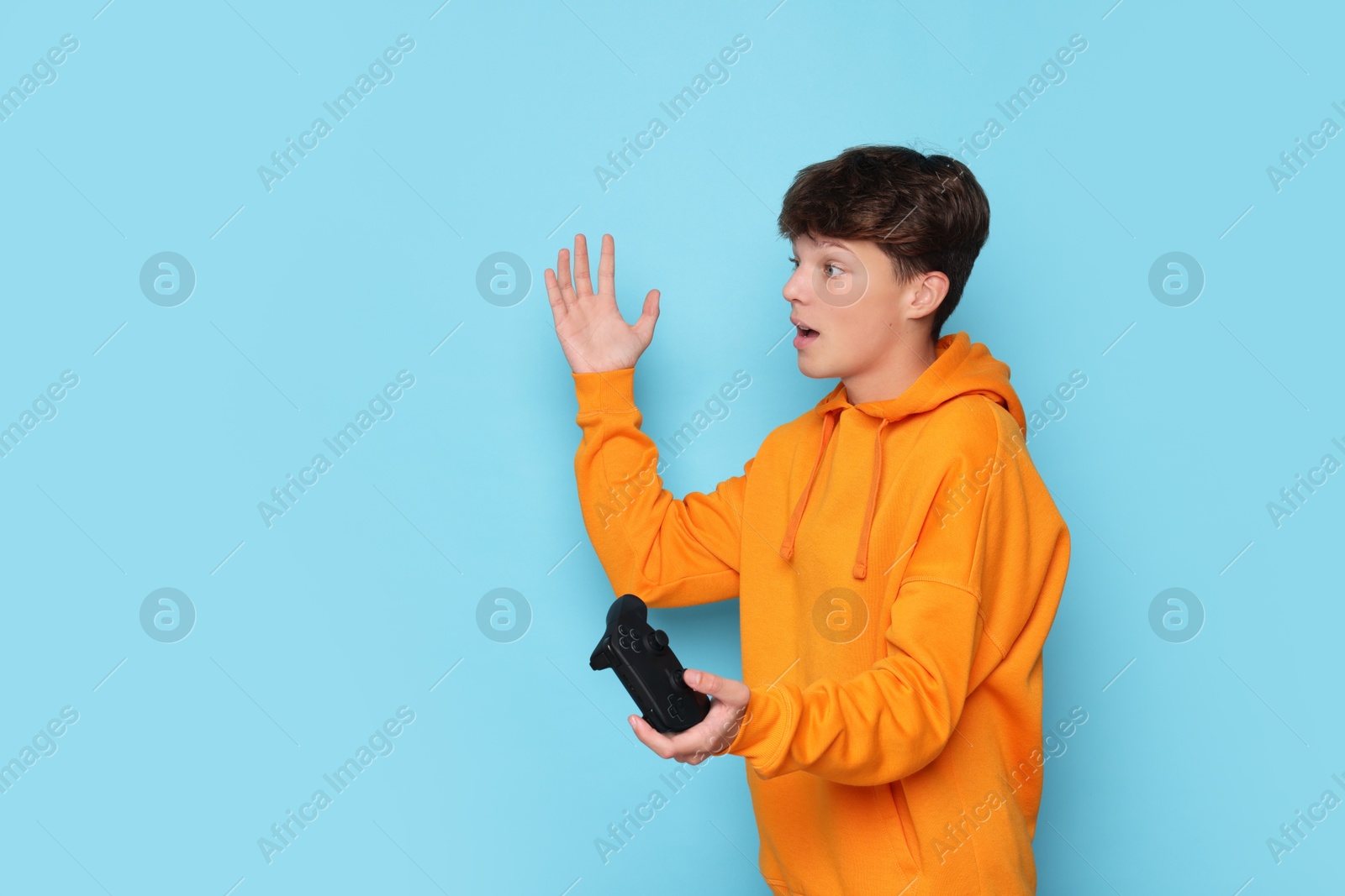 Photo of Emotional teenage boy with controller on light blue background. Space for text