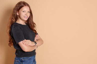 Photo of Smiling teenage girl with crossed arms on beige background. Space for text