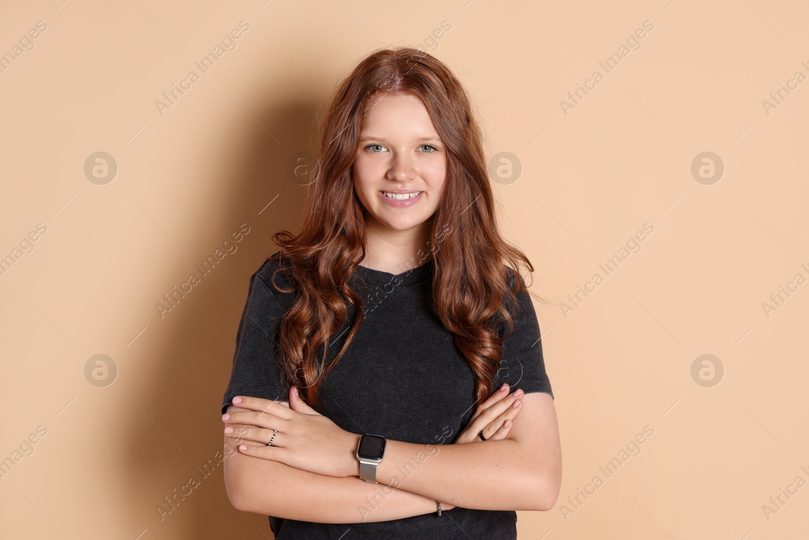 Photo of Smiling teenage girl with crossed arms on beige background