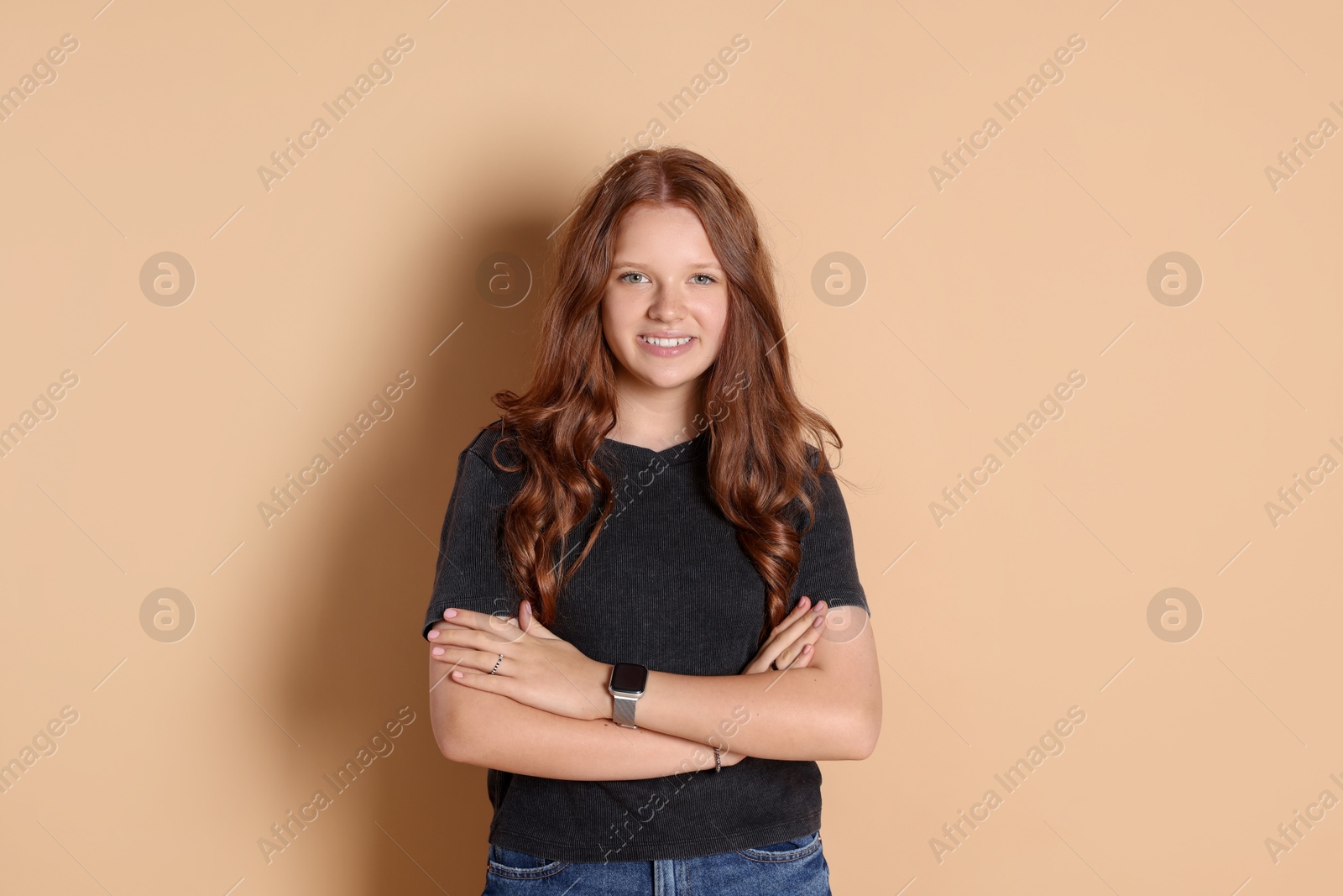 Photo of Smiling teenage girl with crossed arms on beige background