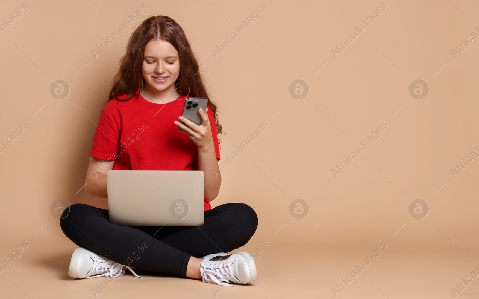 Photo of Smiling teenage girl with laptop and smartphone on beige background. Space for text