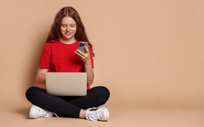 Photo of Smiling teenage girl with laptop and smartphone on beige background. Space for text