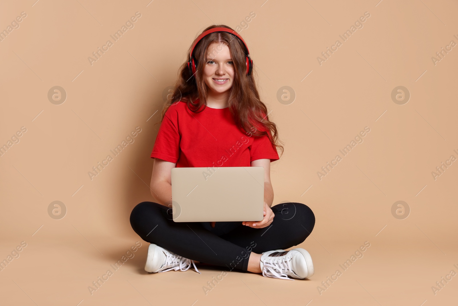 Photo of Smiling teenage girl in headphones with laptop on beige background