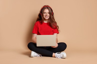 Smiling teenage girl in headphones with laptop on beige background