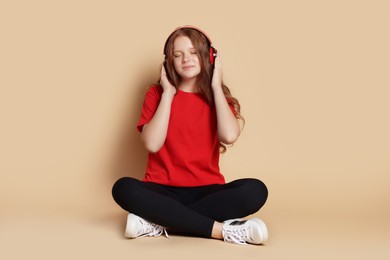 Photo of Cute teenage girl in headphones listening to music on beige background