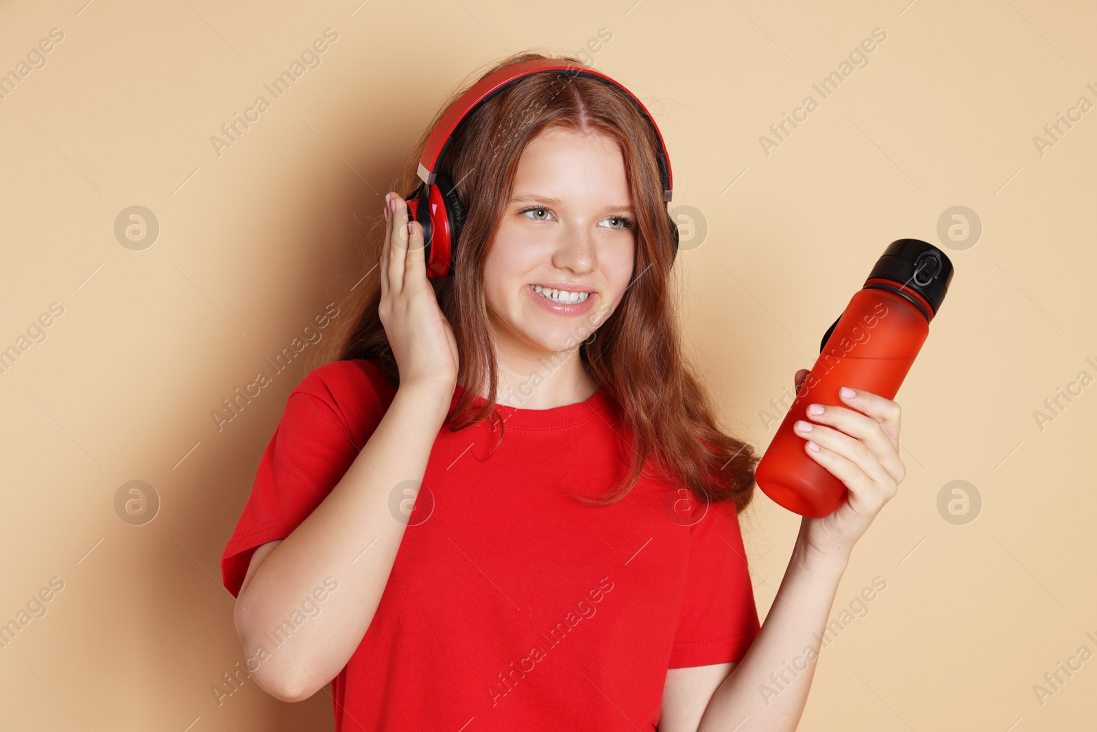 Photo of Smiling teenage girl with bottle listening to music on beige background