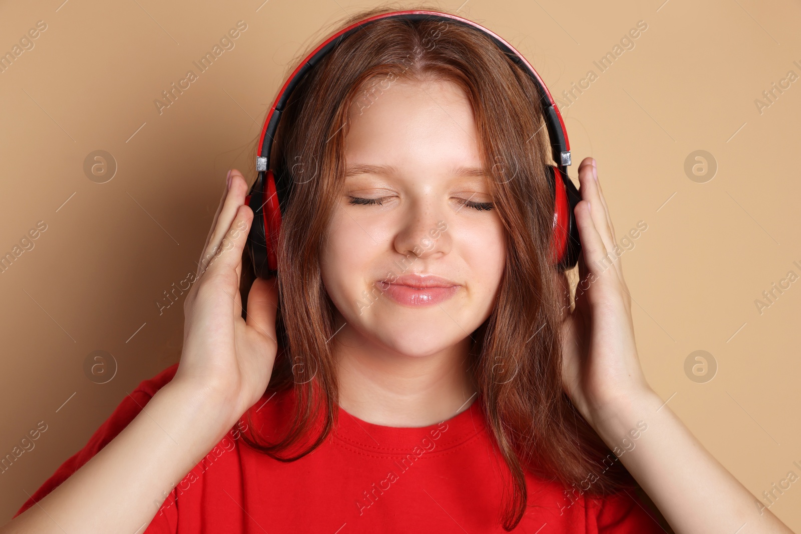 Photo of Cute teenage girl in headphones listening to music on beige background