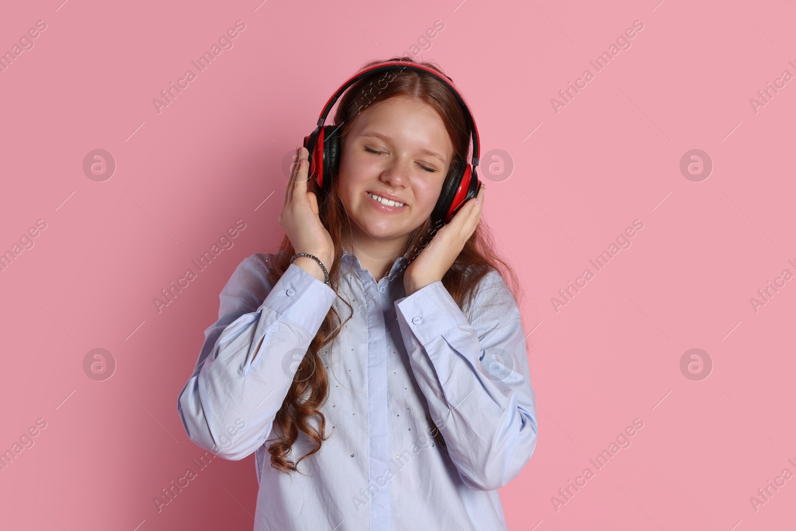 Photo of Smiling teenage girl in headphones listening to music on pink background