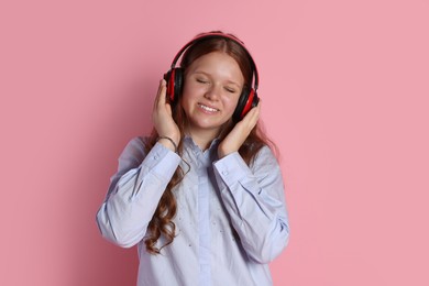 Smiling teenage girl in headphones listening to music on pink background