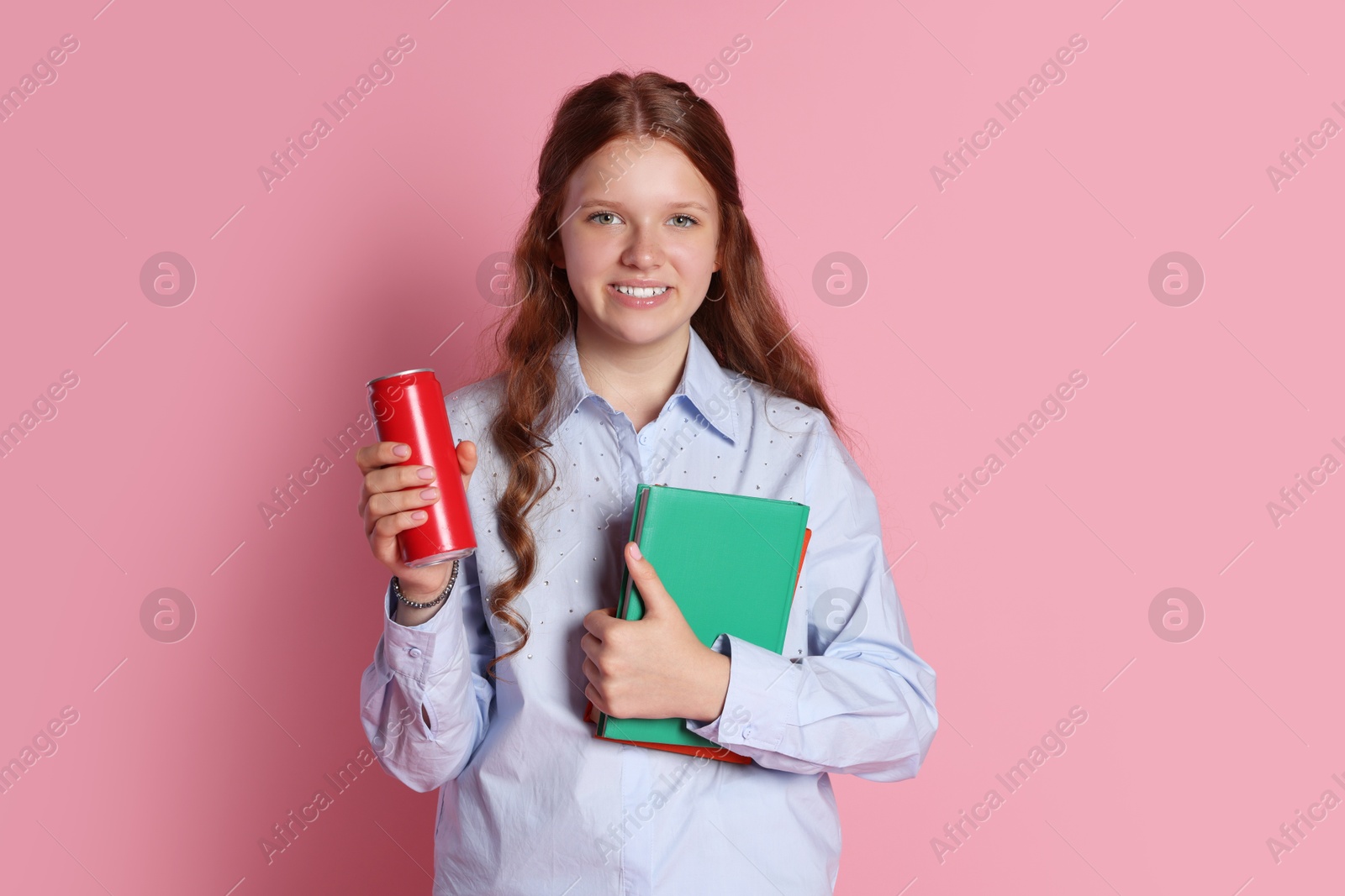 Photo of Smiling teenage girl with books and can on pink background