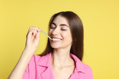 Photo of Young woman eating tasty rainbow sour belt on yellow background