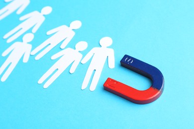 Photo of Magnet attracting paper cutouts of humans on light blue background, closeup