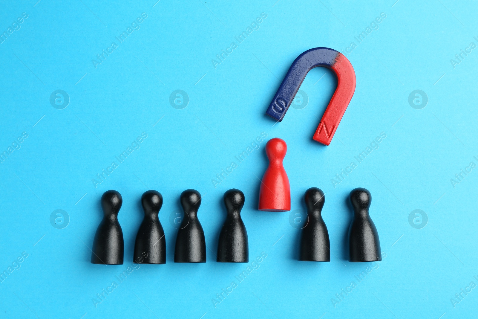 Photo of Magnet attracting human figures on light blue background, flat lay