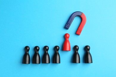 Photo of Magnet attracting human figures on light blue background, flat lay