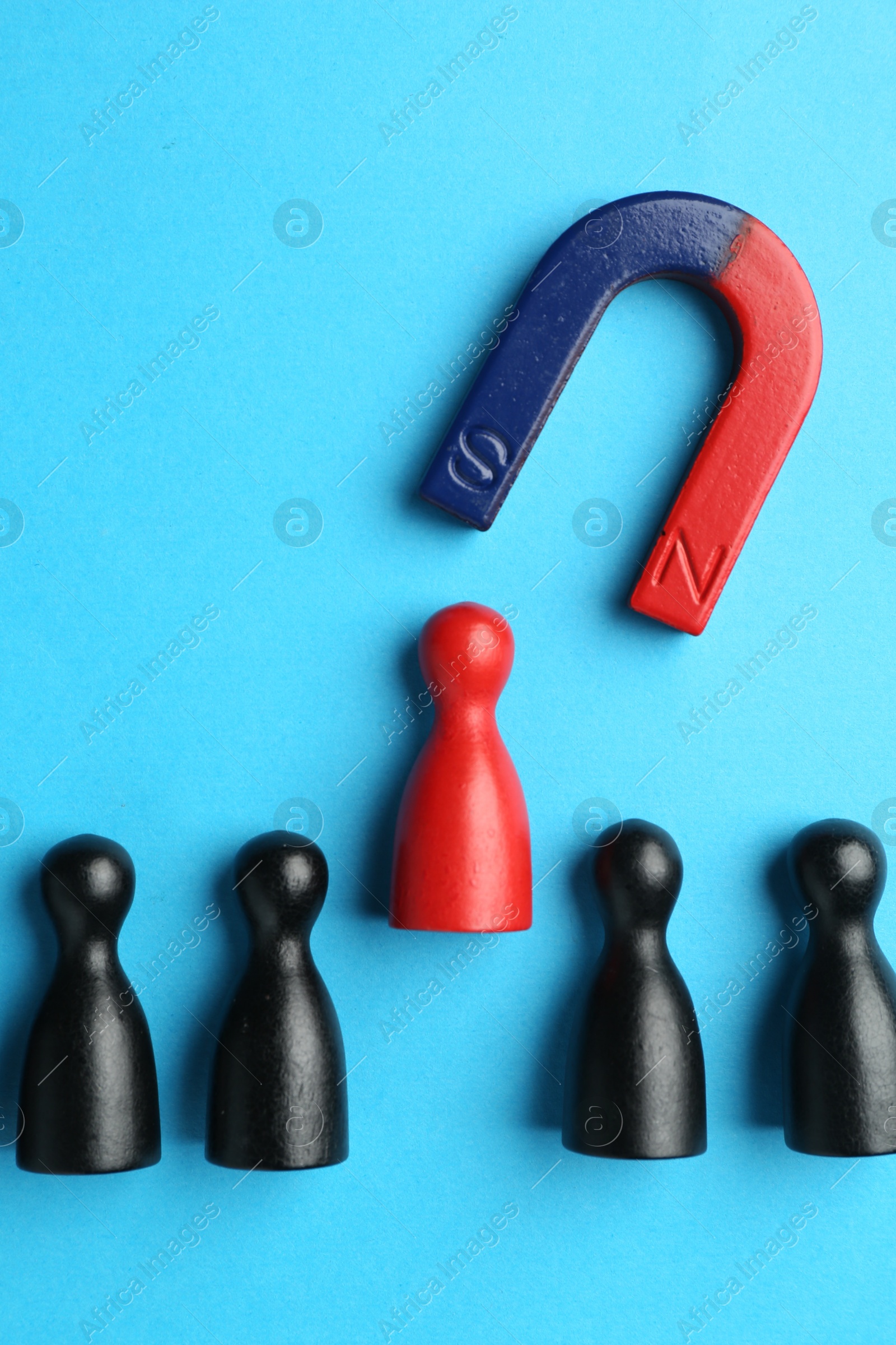 Photo of Magnet attracting human figures on light blue background, flat lay