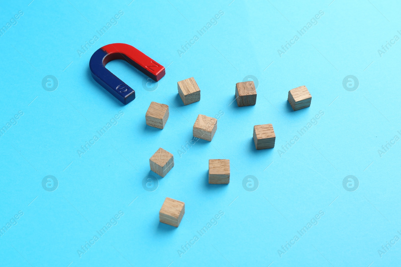 Photo of Magnet attracting wooden cubes on light blue background