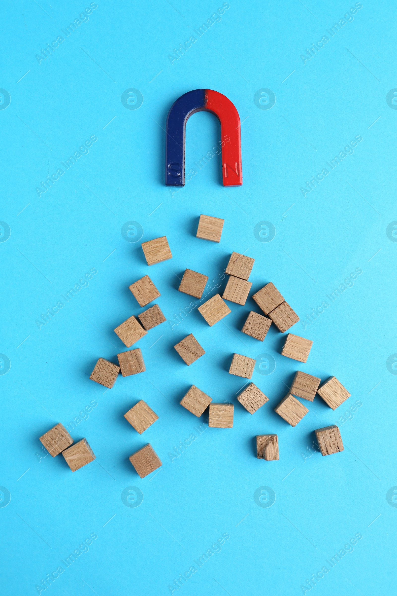 Photo of Magnet attracting wooden cubes on light blue background, flat lay