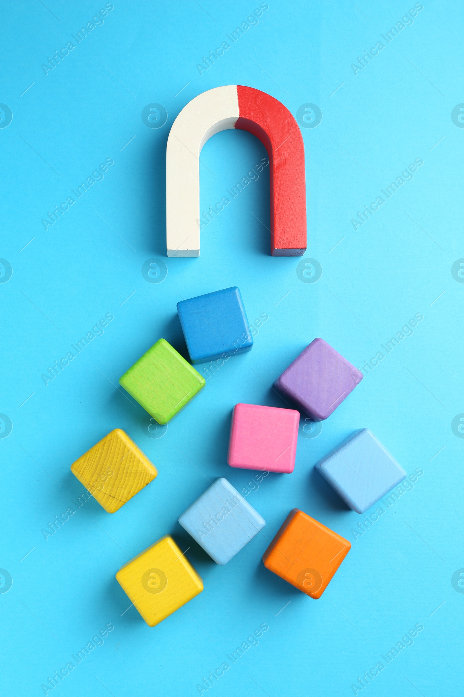 Photo of Magnet attracting colorful cubes on light blue background, flat lay