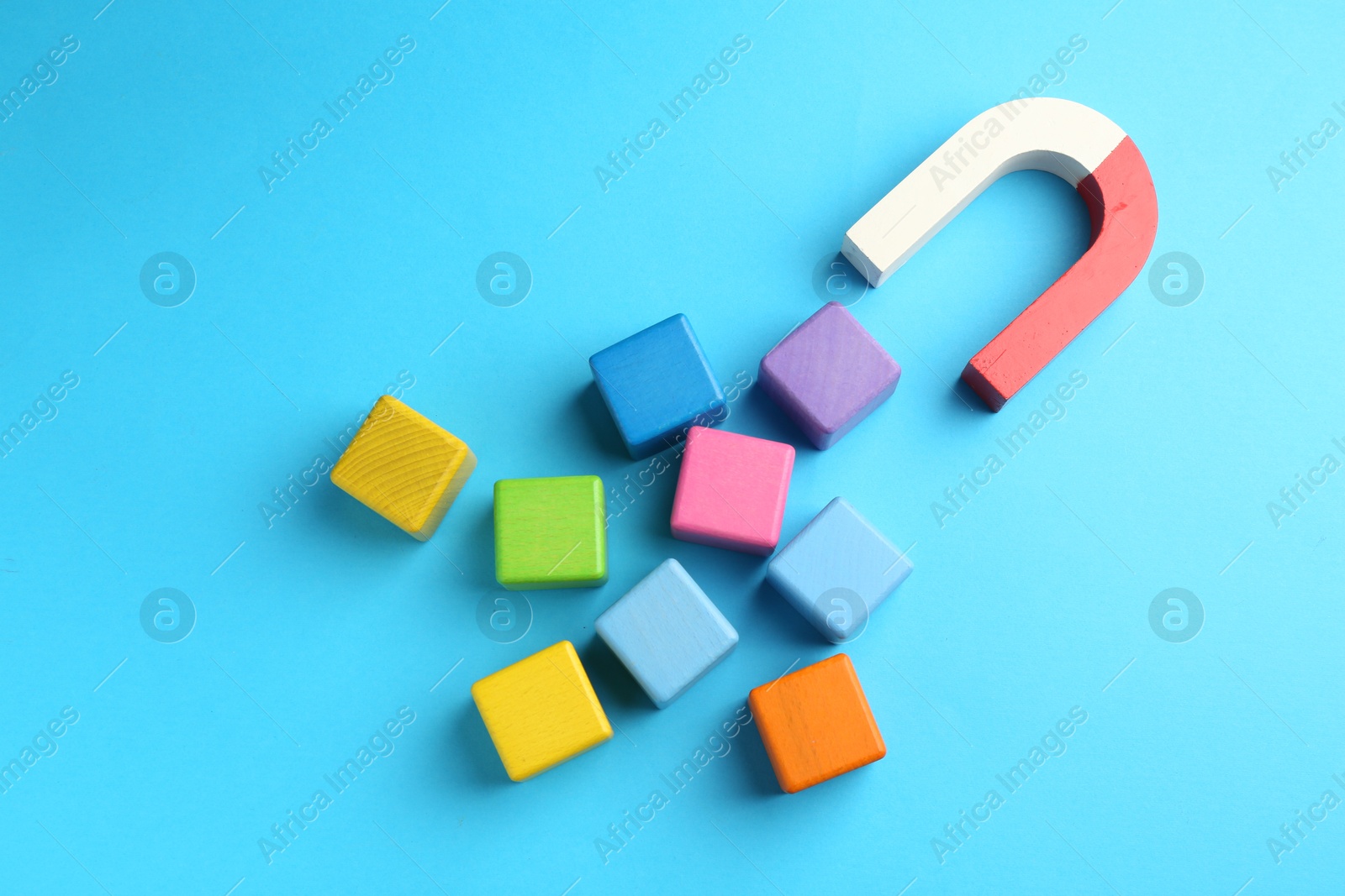 Photo of Magnet attracting colorful cubes on light blue background, flat lay