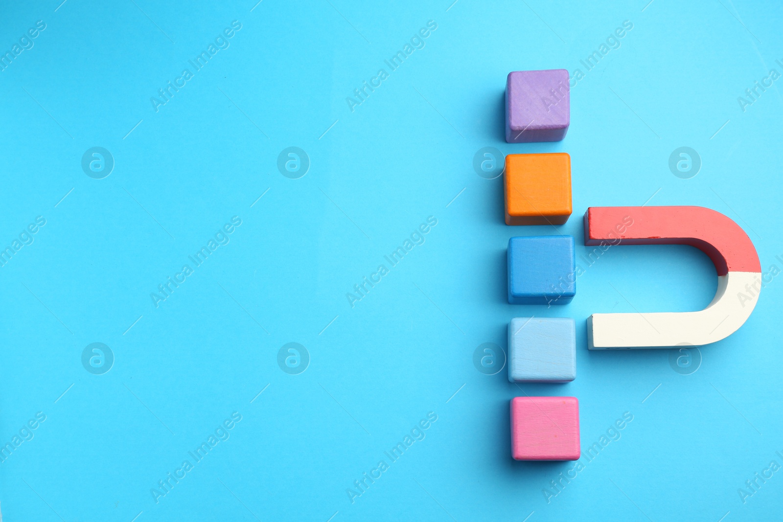 Photo of Magnet attracting colorful cubes on light blue background, flat lay. Space for text