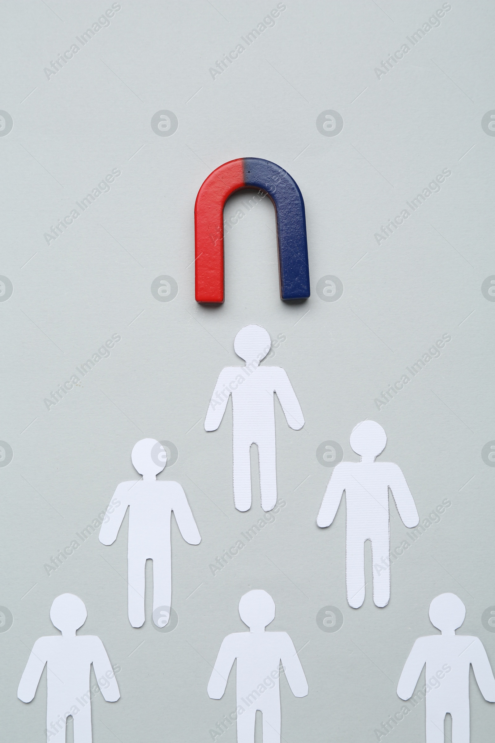 Photo of Magnet attracting paper cutouts of humans on light grey background, flat lay