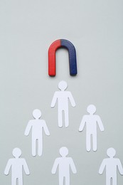 Photo of Magnet attracting paper cutouts of humans on light grey background, flat lay