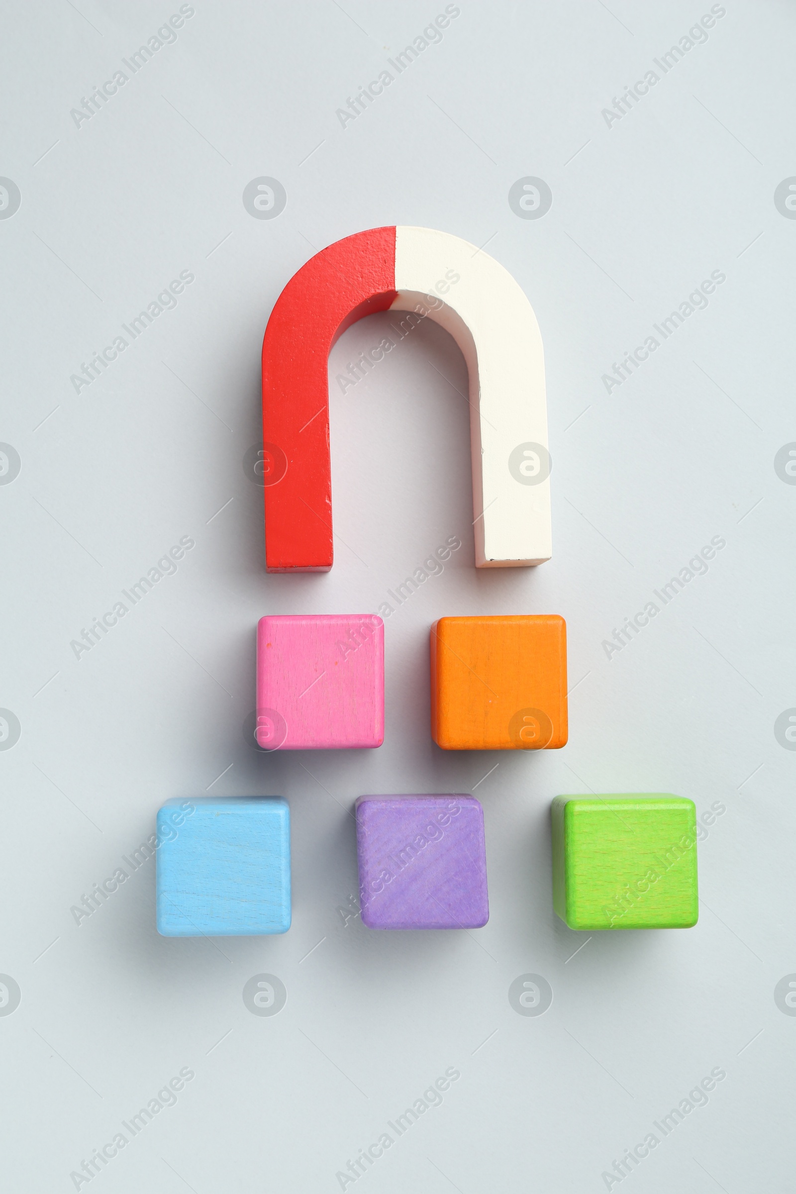 Photo of Magnet attracting colorful cubes on light grey background, flat lay