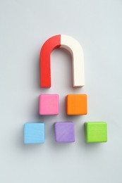 Photo of Magnet attracting colorful cubes on light grey background, flat lay