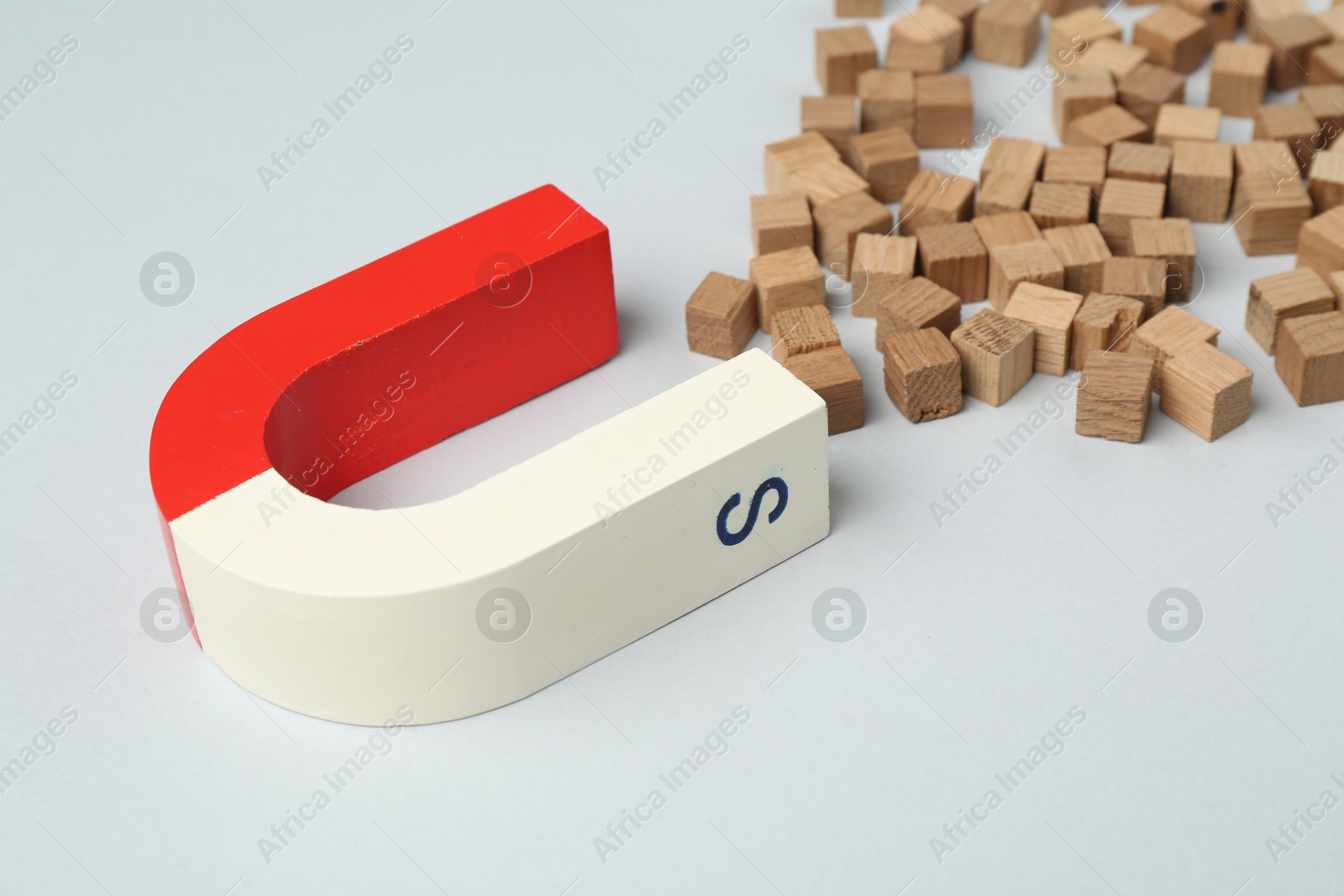 Photo of Magnet attracting wooden cubes on light grey background, closeup