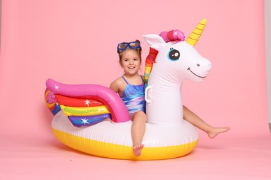 Photo of Cute little girl in swimsuit with unicorn pool float on light pink background