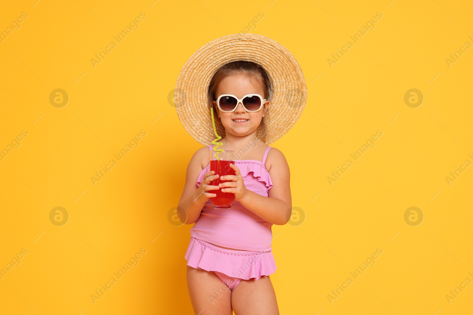 Photo of Cute little girl in swimsuit and straw hat with drink on orange background