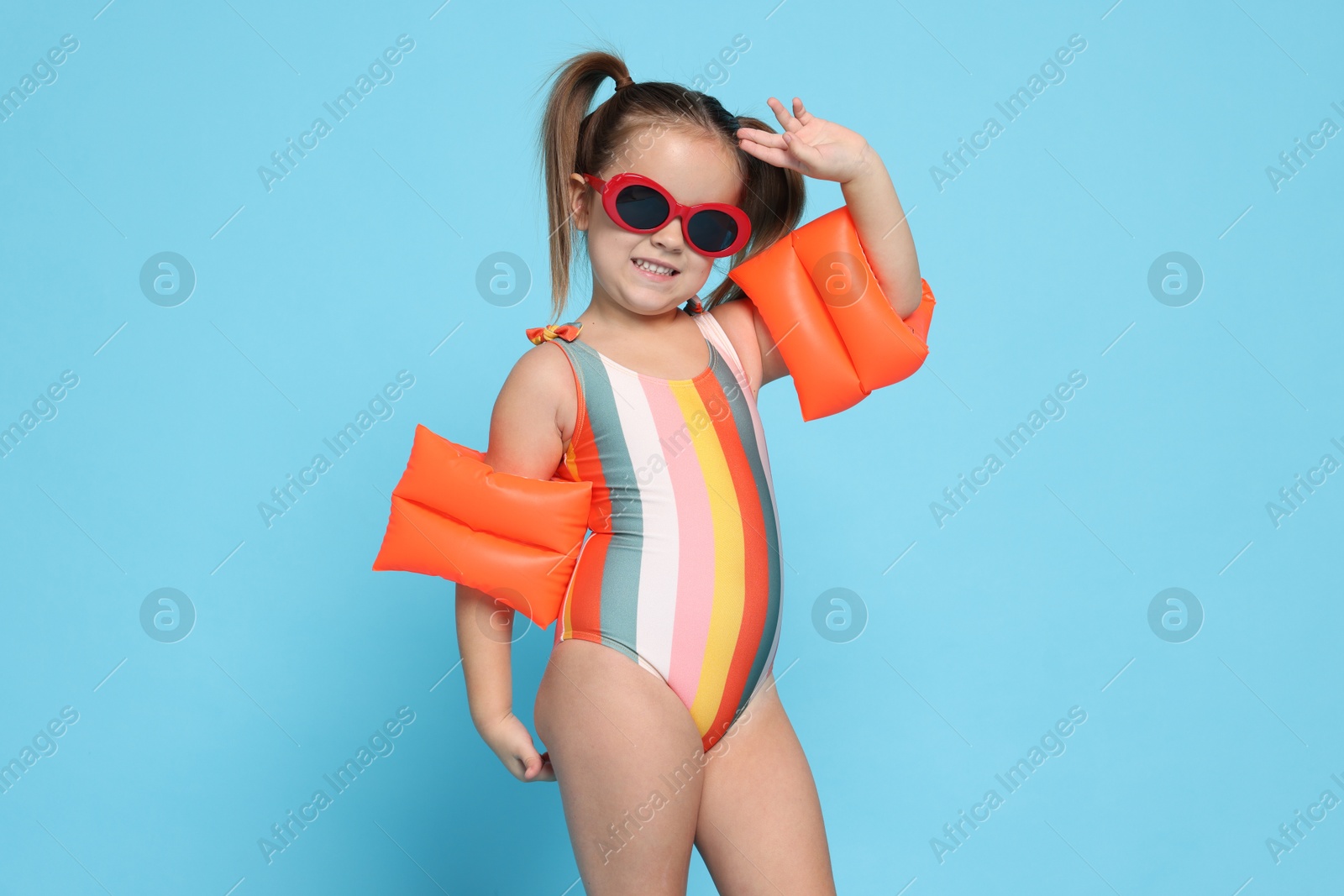 Photo of Cute little girl in swimsuit with swim armbands on light blue background