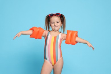 Photo of Cute little girl in swimsuit with swim armbands on light blue background