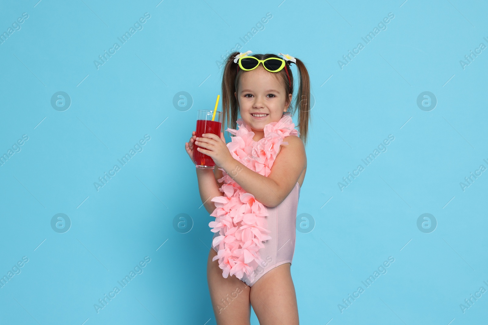 Photo of Cute little girl in swimsuit with drink on light blue background