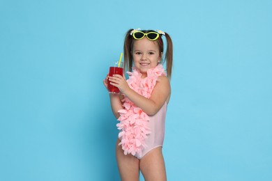 Photo of Cute little girl in swimsuit with drink on light blue background