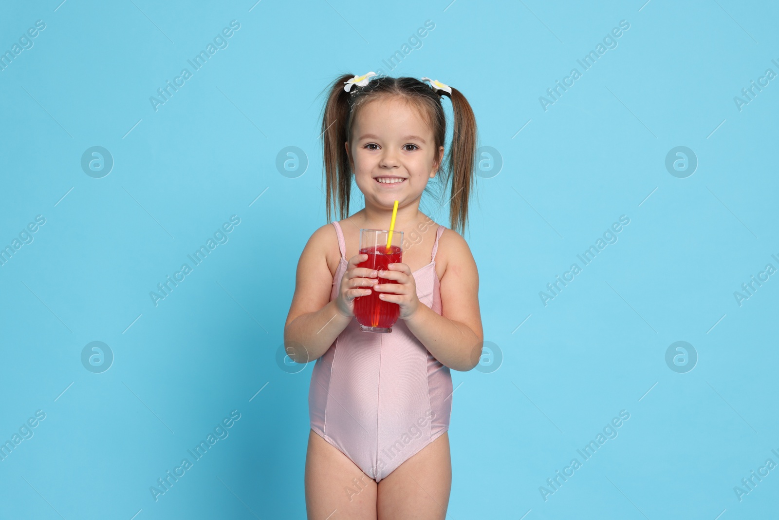 Photo of Cute little girl in swimsuit with drink on light blue background