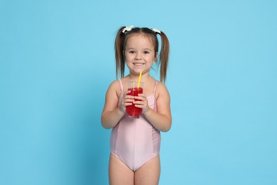 Cute little girl in swimsuit with drink on light blue background