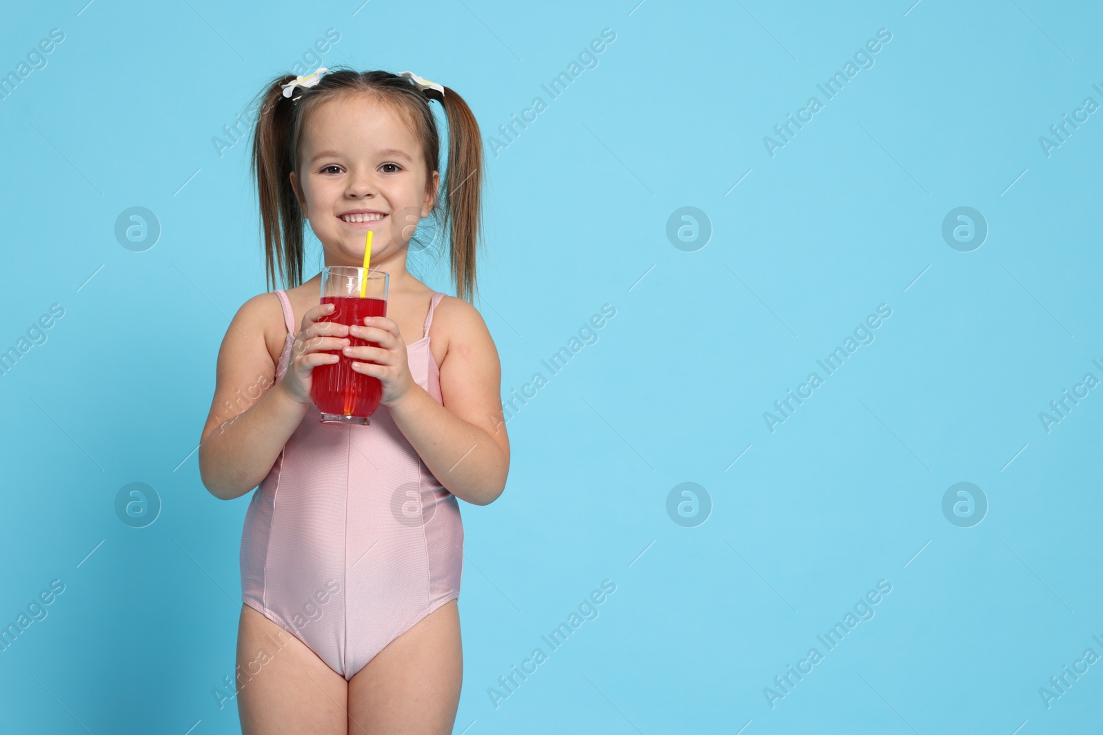 Photo of Cute little girl in swimsuit with drink on light blue background. Space for text