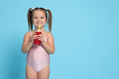 Photo of Cute little girl in swimsuit with drink on light blue background. Space for text