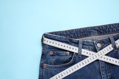 Photo of Jeans and measuring tape on light blue background, top view. Space for text