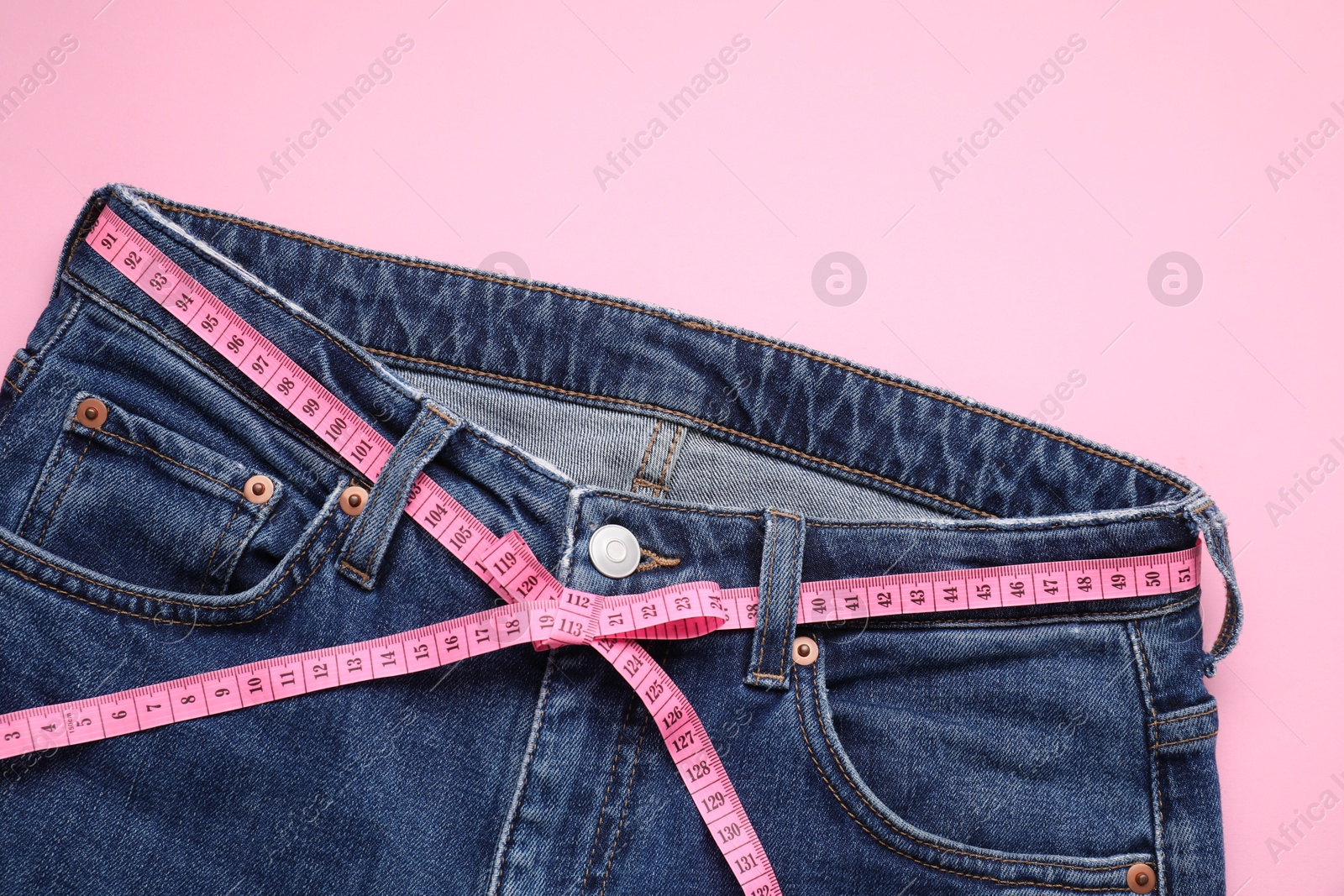 Photo of Jeans and measuring tape on pink background, top view