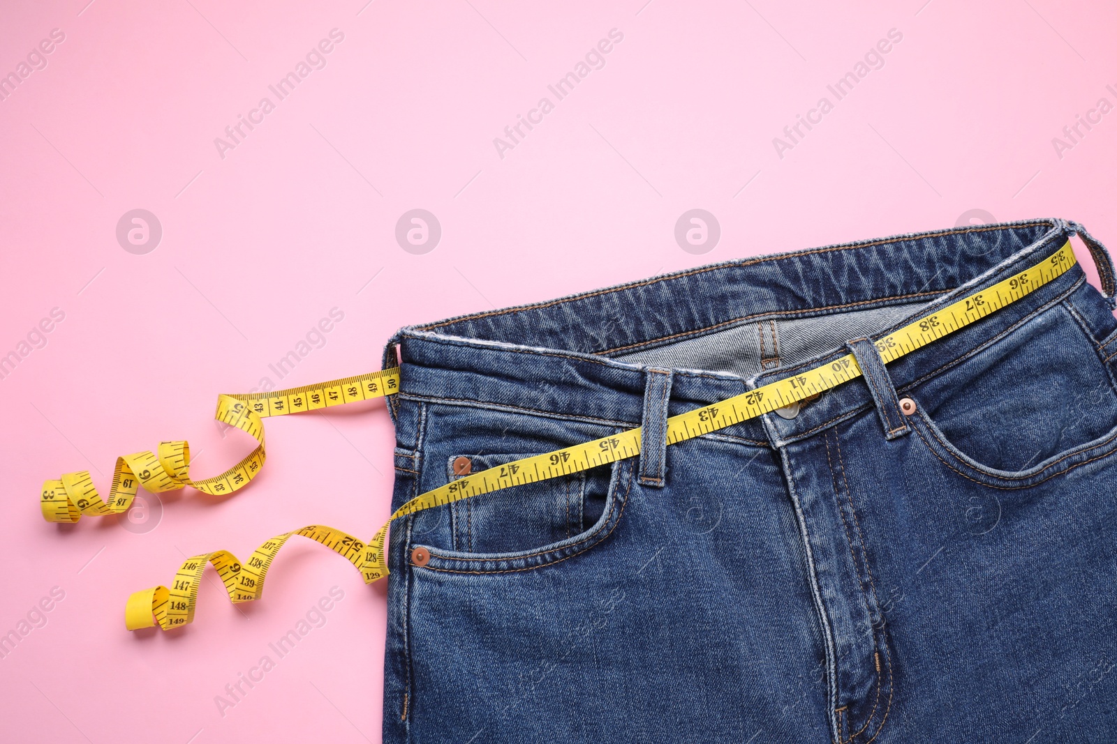 Photo of Jeans and measuring tape on pink background, top view