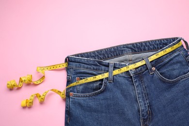 Photo of Jeans and measuring tape on pink background, top view