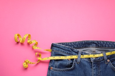 Photo of Jeans and measuring tape on pink background, top view. Space for text