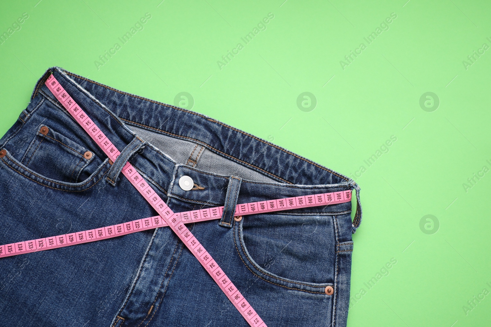 Photo of Jeans and measuring tape on light green background, top view. Space for text