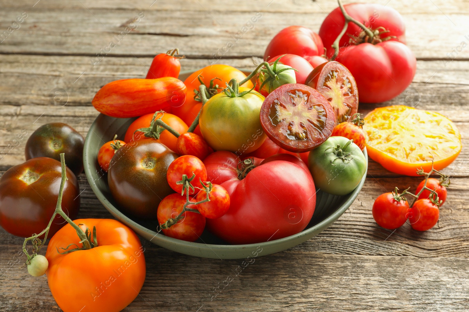 Photo of Different ripe tomatoes in bowl on wooden table